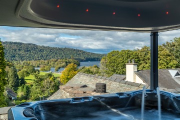 Covered outdoor hot tub overlooking a lake and green hills, with private seating and elevated countryside views